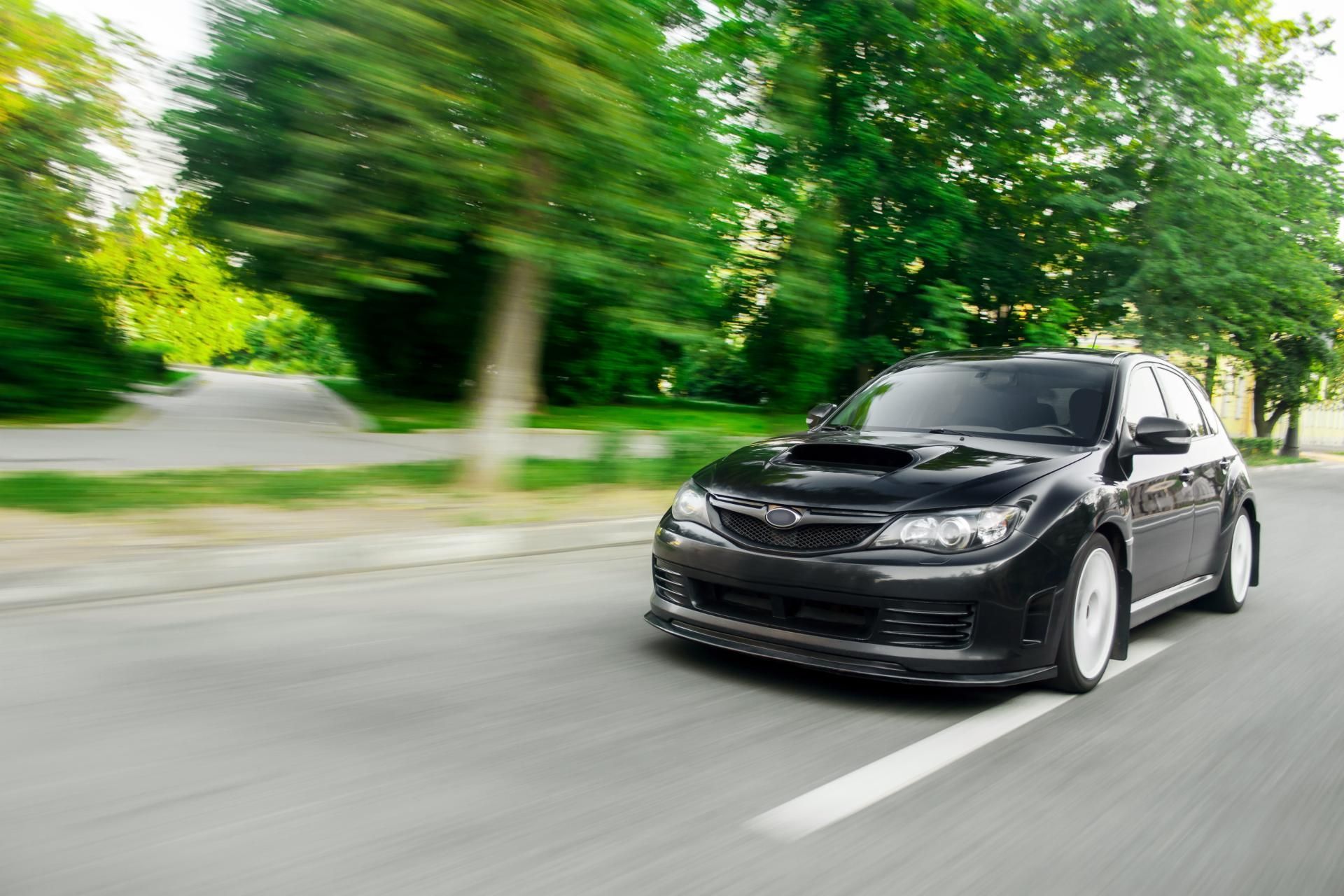 Black compact car driving on a tree-lined road with motion blur in the background