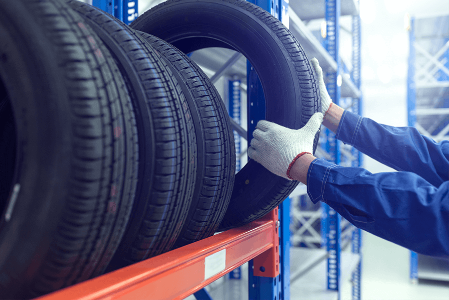 Gloved hands inspecting large black tires on an orange warehouse rack