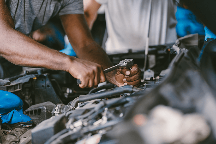 Mechanic working under an open car hood with tools in a garage