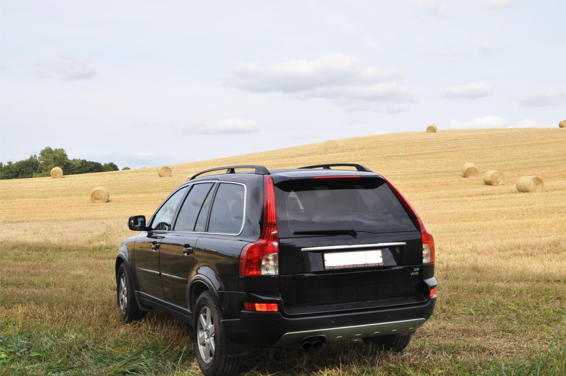 Black SUV parked on grass beside a golden field under a cloudy sky