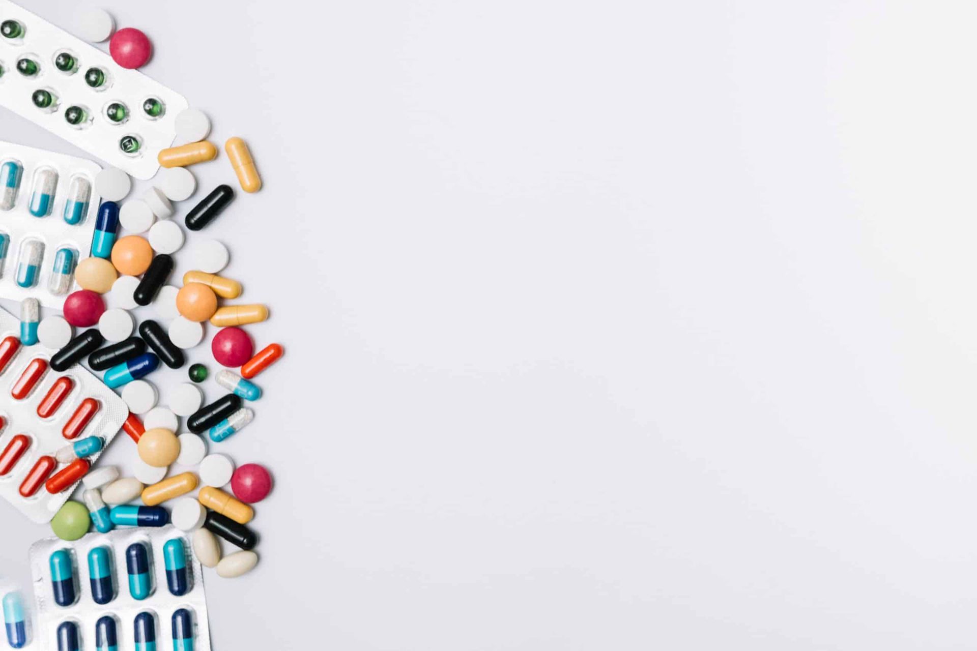 Pills and capsules of various colors scattered on a white background, likely for medical or health-related use.