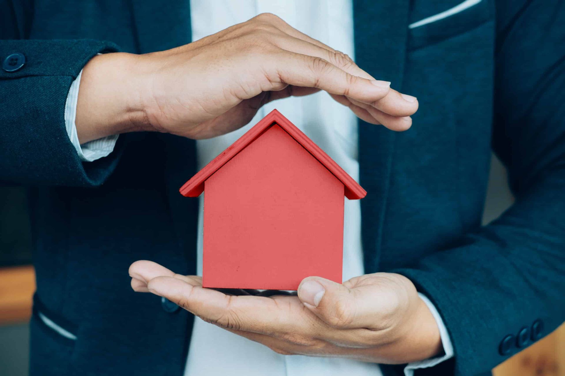 Hands holding a red house, symbolizing protection.