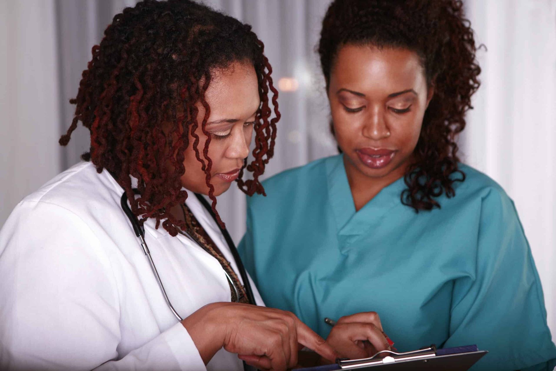 Doctor in white coat and nurse in teal scrubs looking at chart together.