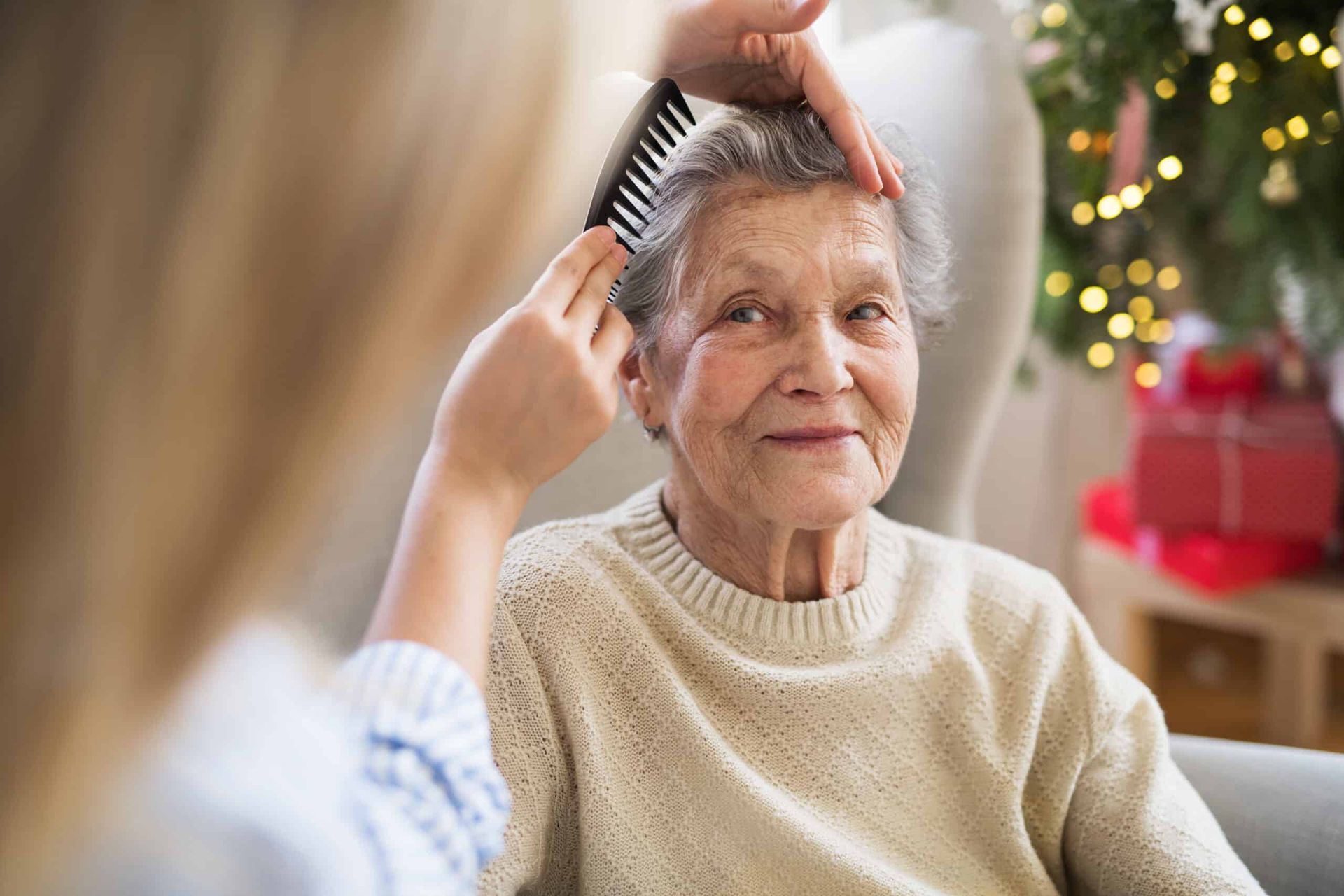 Woman having her hair combed by another person; Christmas tree in background.