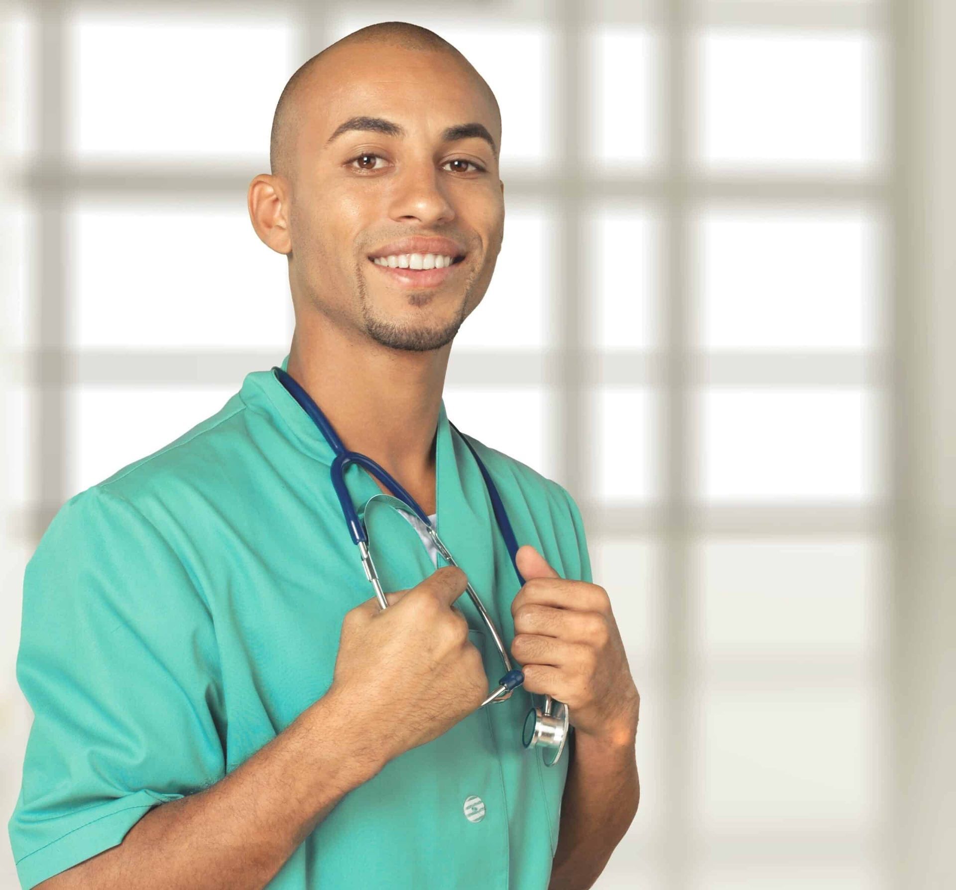 Smiling Black male doctor in scrubs, stethoscope around neck, in a medical setting.