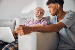Older man and younger man smiling together while looking at a laptop on a couch.
