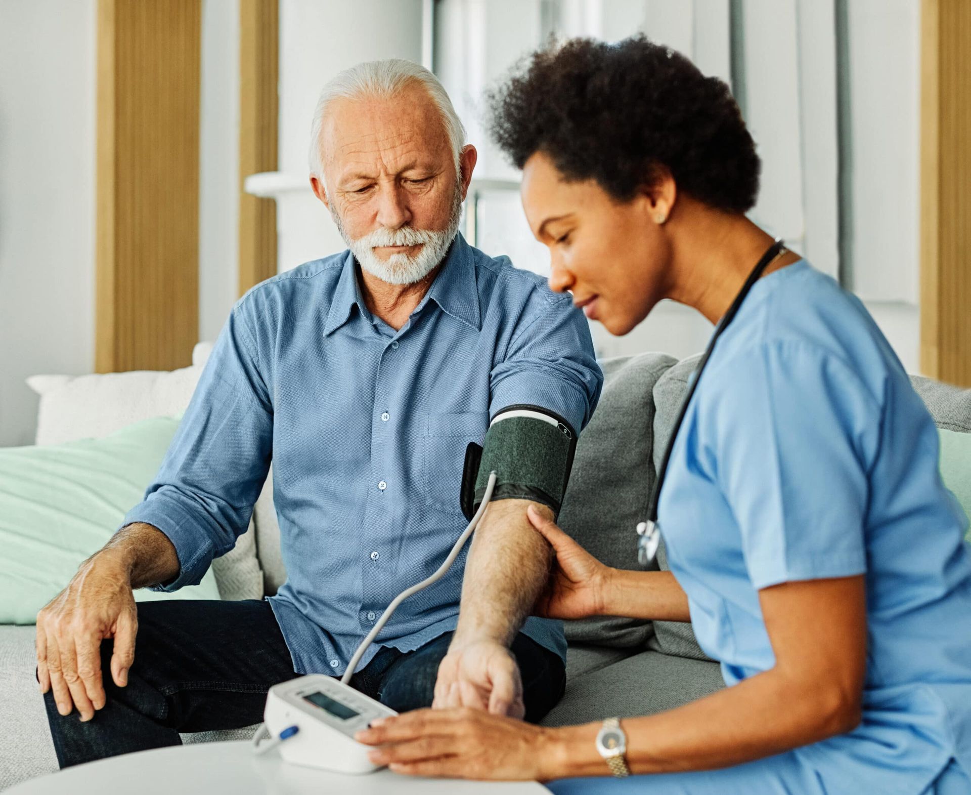 Elderly man has blood pressure checked by a healthcare worker indoors.