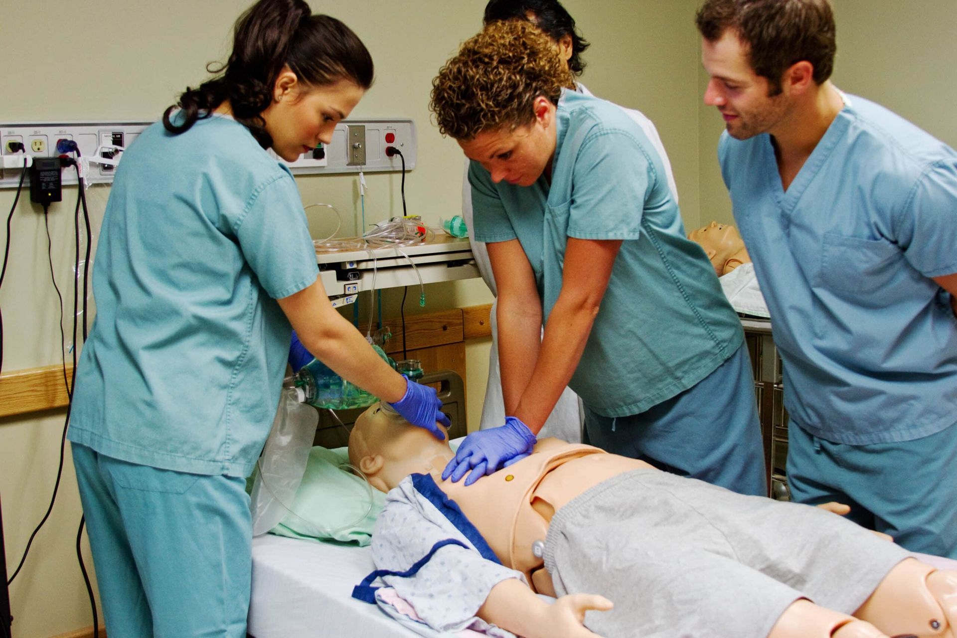 Medical professionals practice CPR on a mannequin in a hospital room.