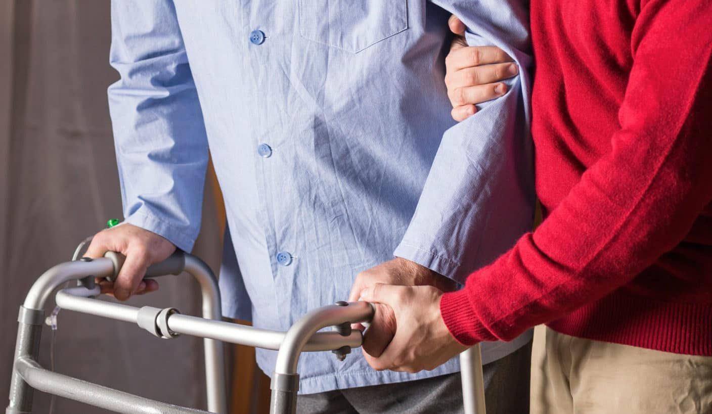 Person using a walker, assisted by someone in a red sweater.