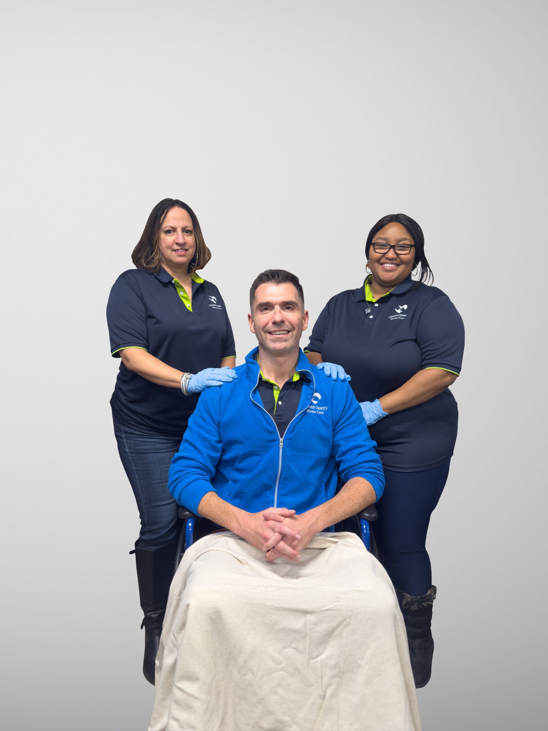 Three healthcare workers, two women and a man in a wheelchair, smiling.
