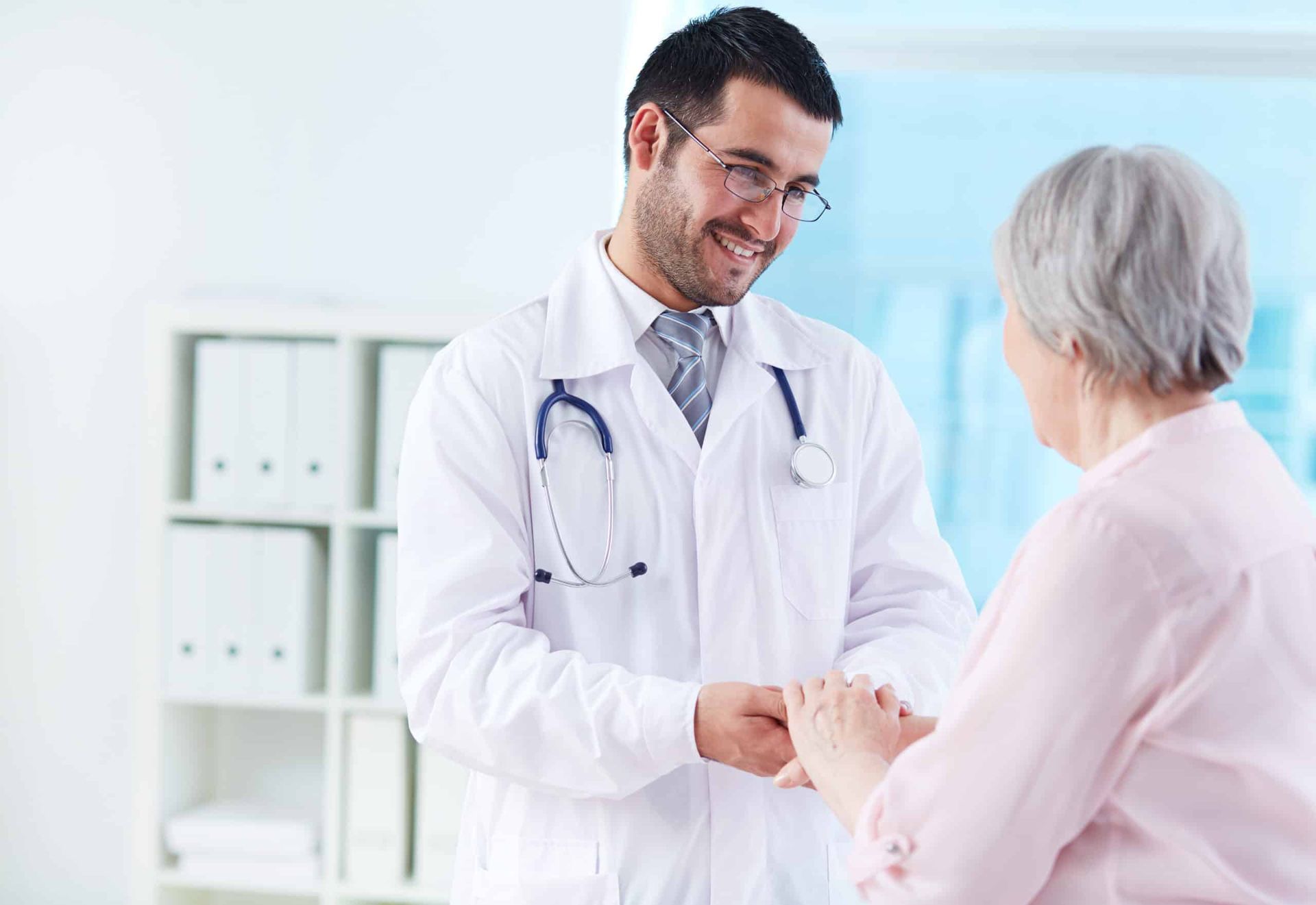 Smiling doctor holding hands with elderly patient in a medical office.
