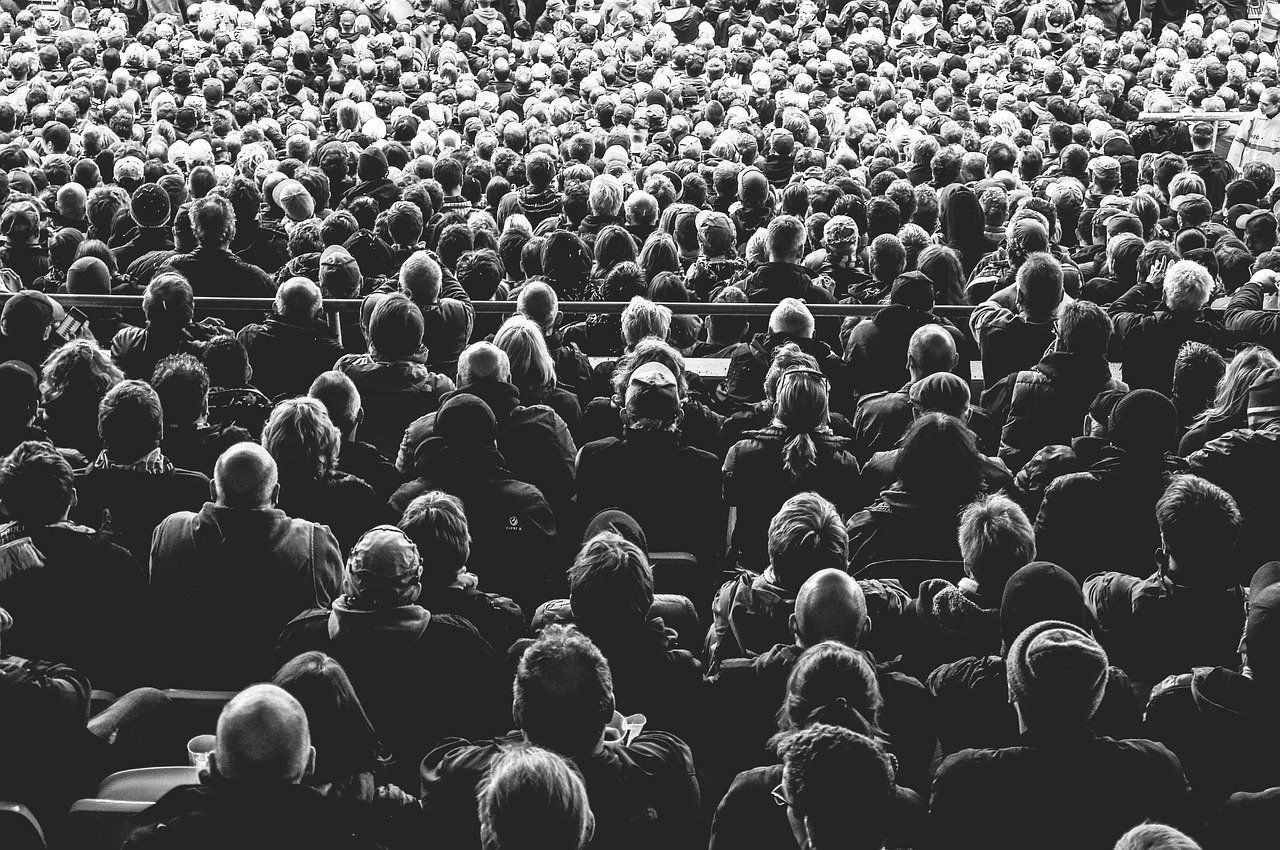 Black and white shot of a large crowd, mostly from the back, in a stadium or similar seating.