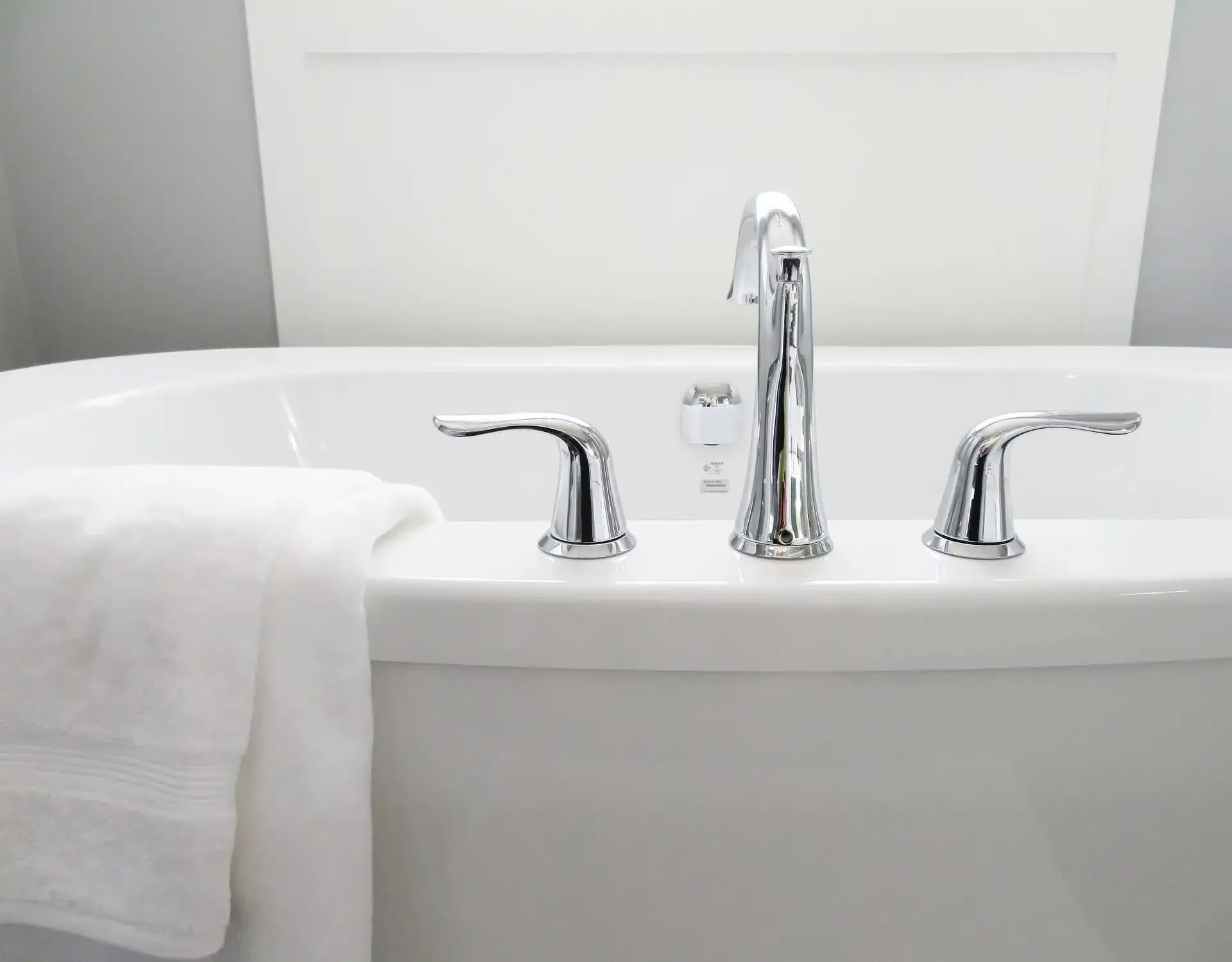 White bathtub with chrome faucet and handles, a white towel hangs on the edge.