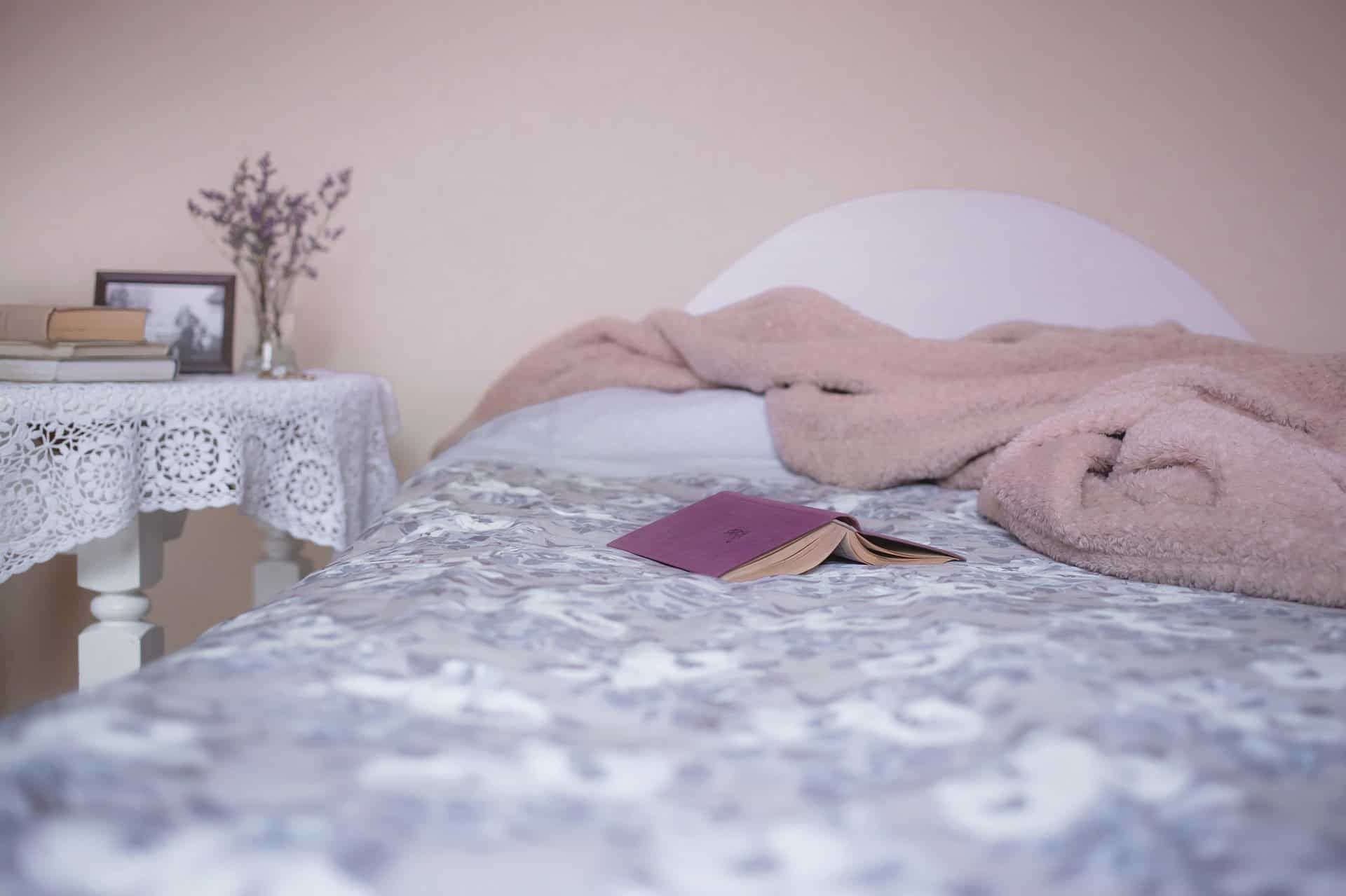 A bed with a floral patterned quilt and a book. A small table with flowers and a photo. Soft pinks.
