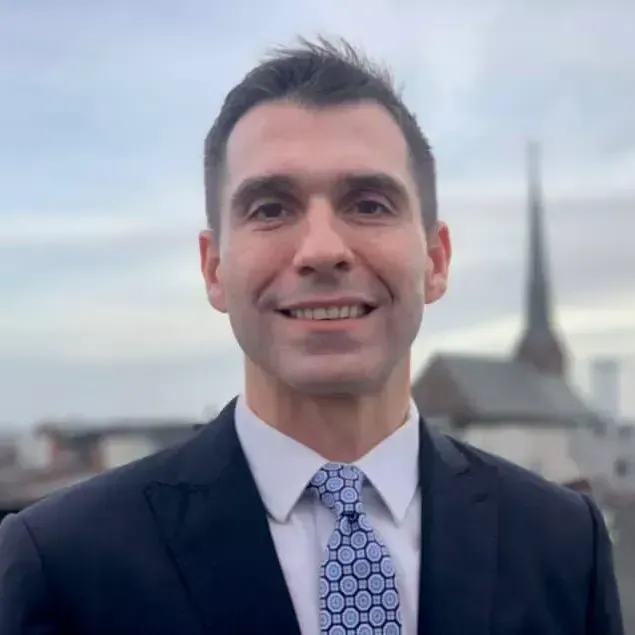 Man in suit smiles, standing on a rooftop with church steeple in background.
