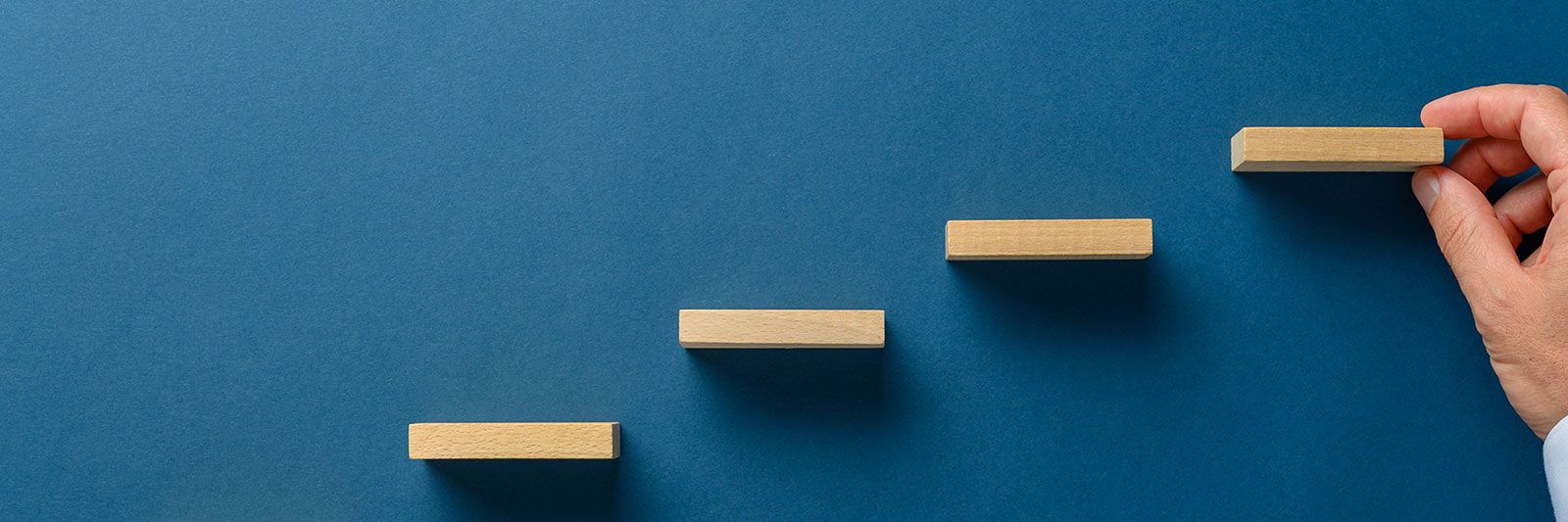 Hand placing a wooden block to complete steps on a blue background.