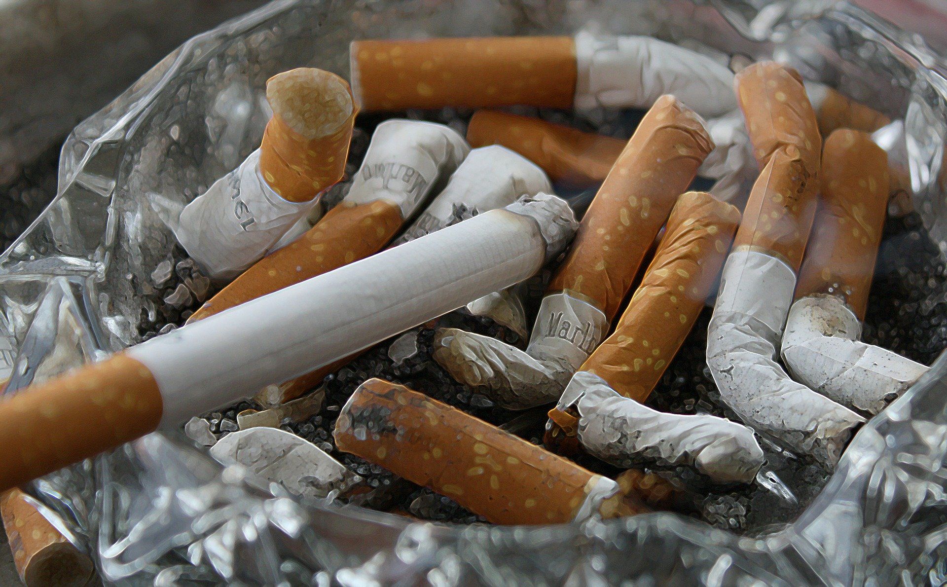 Cigarette butts in a silver ashtray, with one lit cigarette on top.