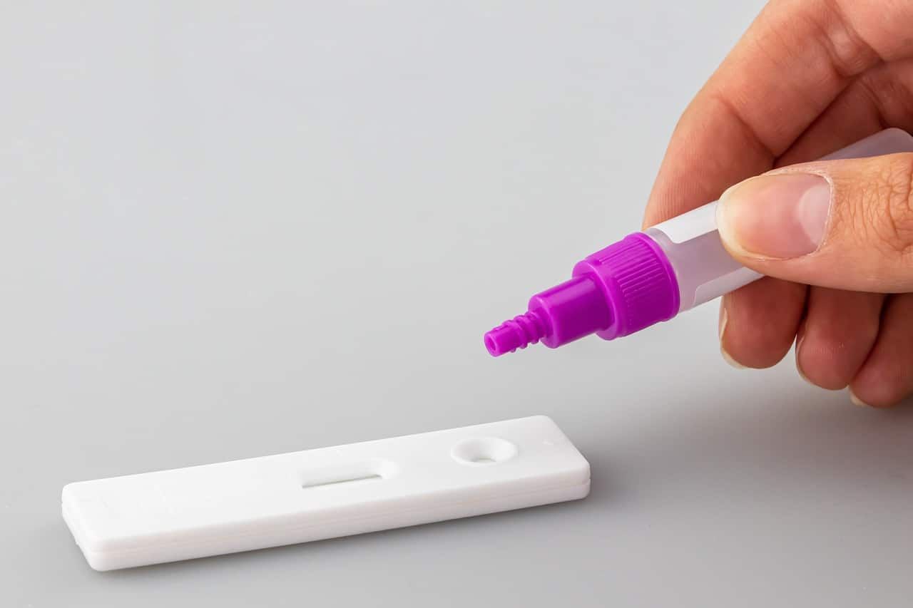 Person holding a purple-tipped dropper above a white test strip on a gray surface.