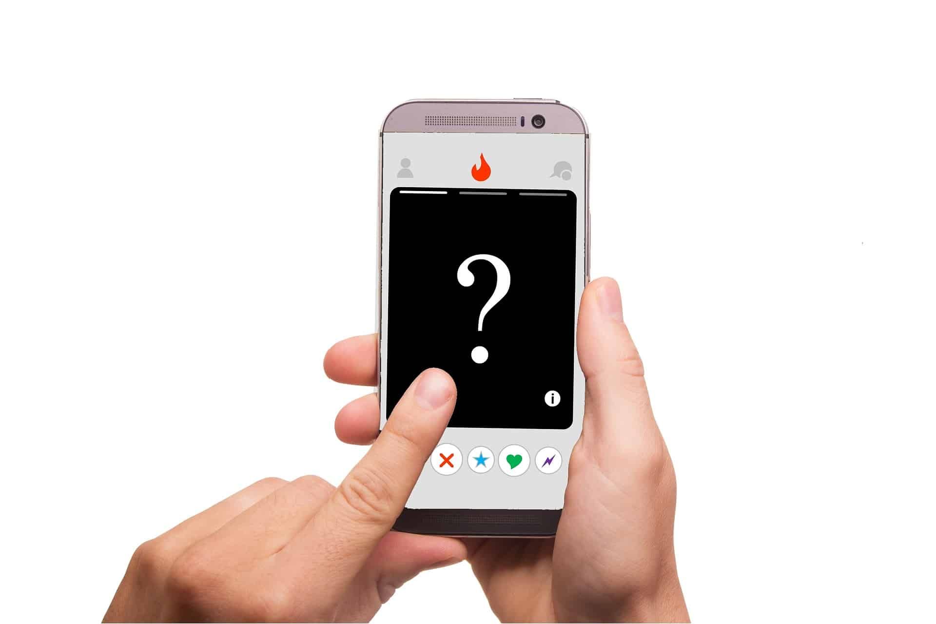Person holding a smartphone with a dating app interface; a finger is tapping the screen with a question mark overlay.
