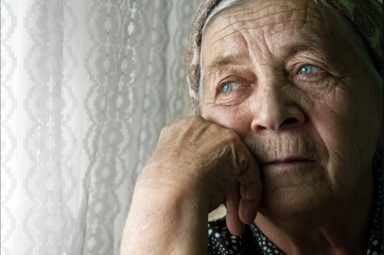 Elderly woman with head resting on hand, gazing out window.