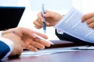 Two people in business suits reviewing paperwork, one hand holding pen.