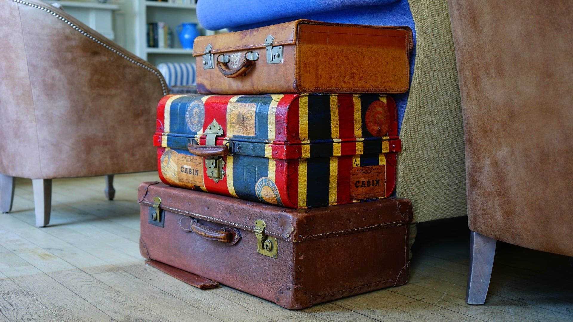 Three vintage suitcases stacked, brown leather and colorful designs.