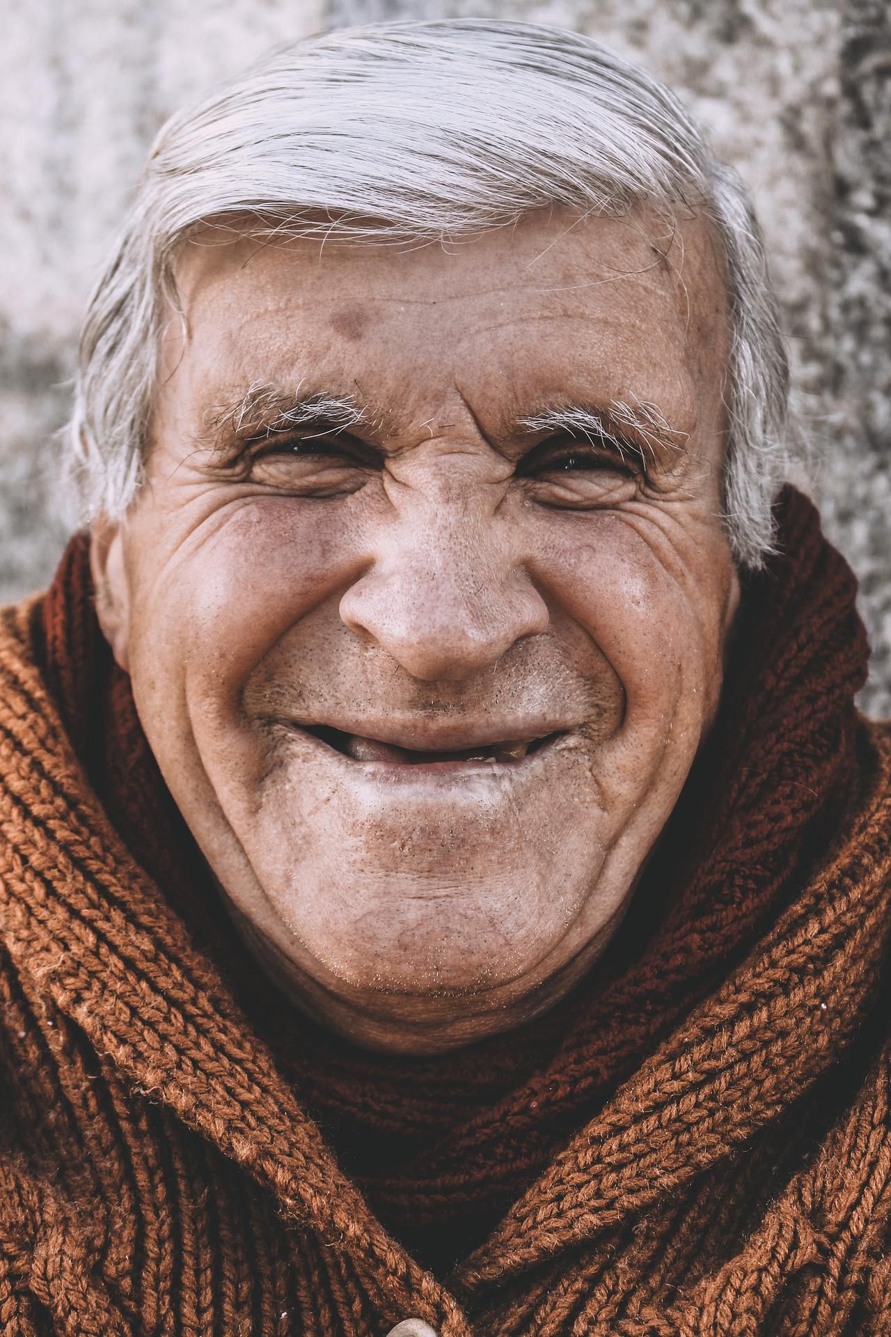 Smiling elderly man with gray hair and brown sweater.