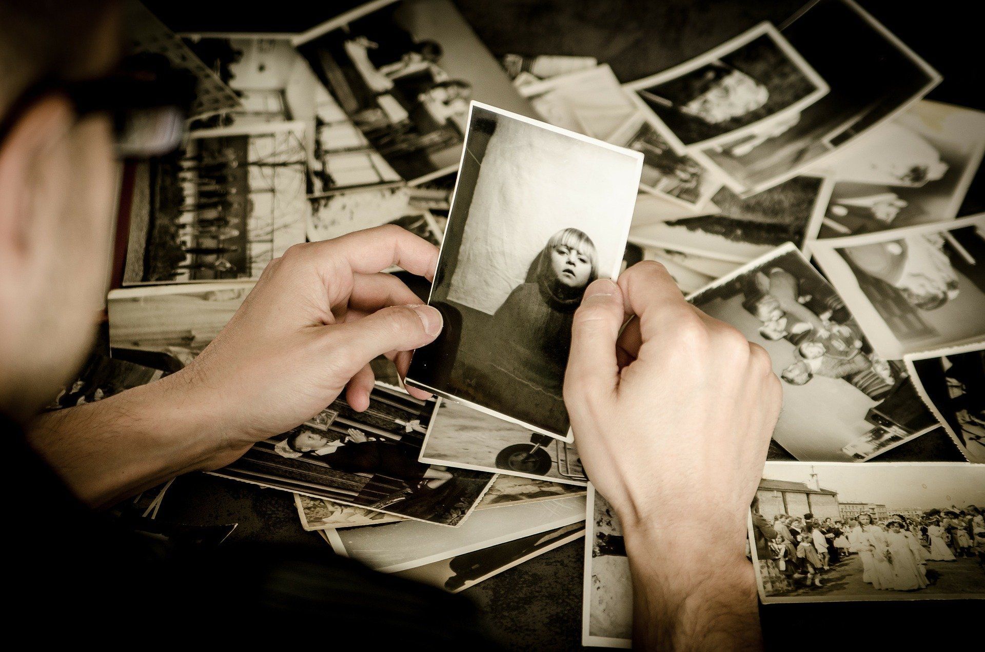 Man examines a black and white photo amongst a pile. Soft focus; nostalgic feel.