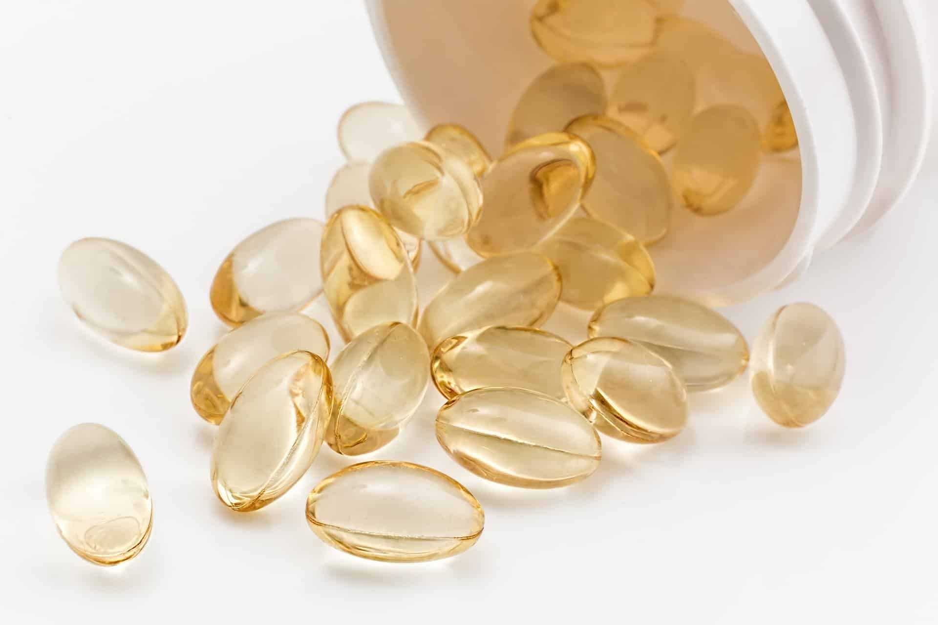 Soft, yellow gel capsules spilling from a white bottle on a white surface.