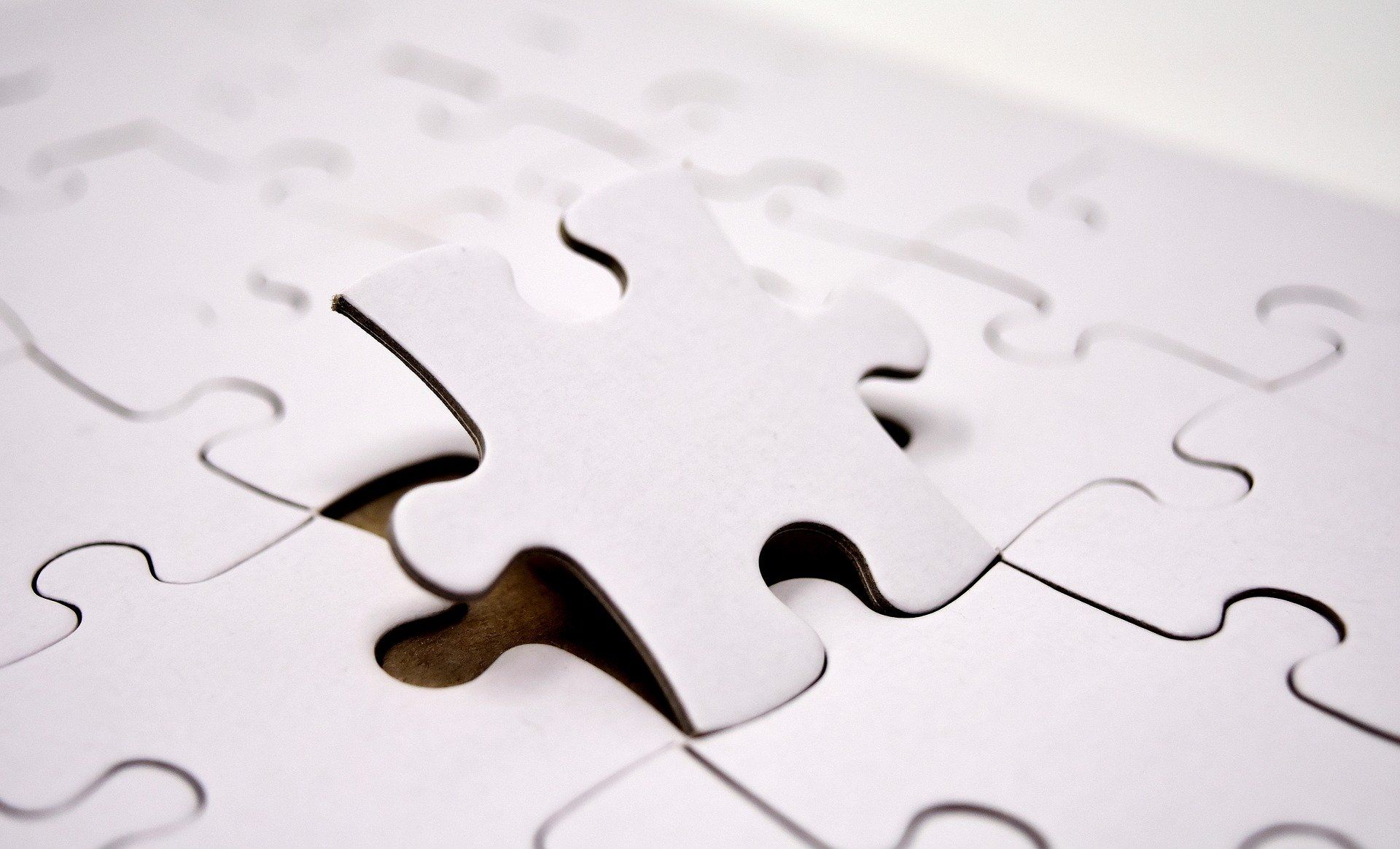White puzzle with one piece slightly lifted, ready to be placed.
