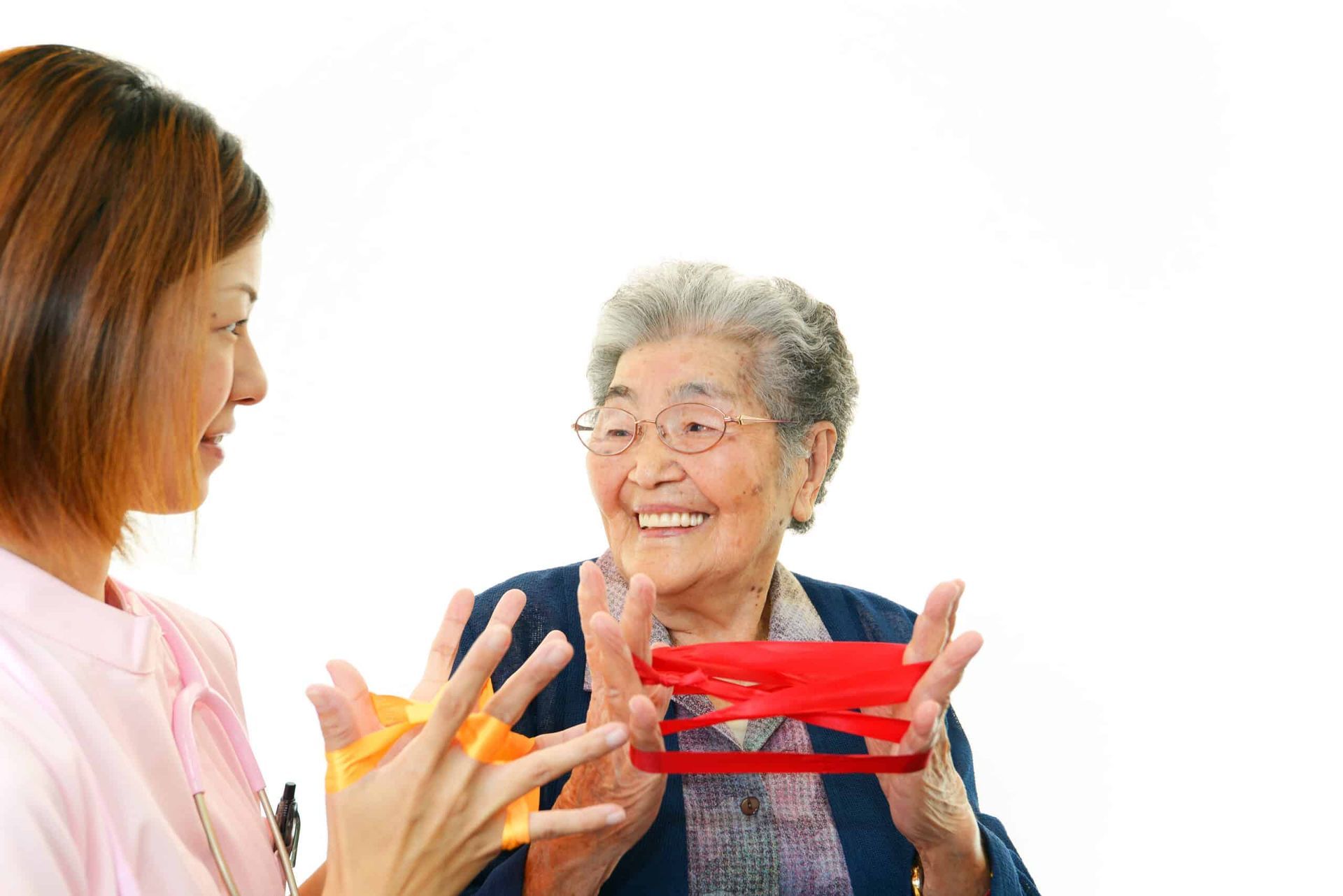 Nurse assisting elderly woman with red and yellow resistance bands, both smiling.