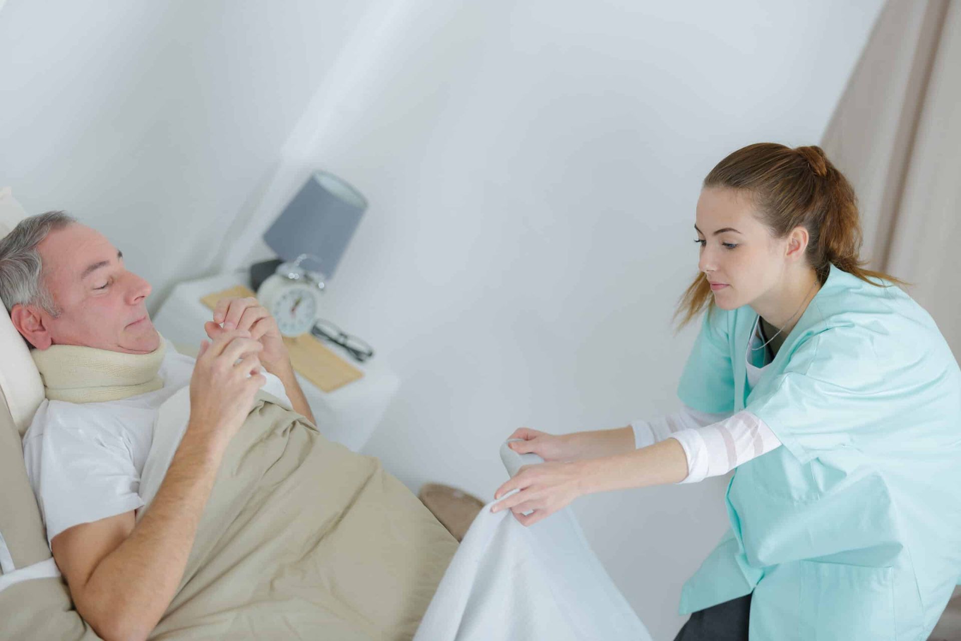 Nurse assisting a man in bed with a neck brace, adjusting a blanket.