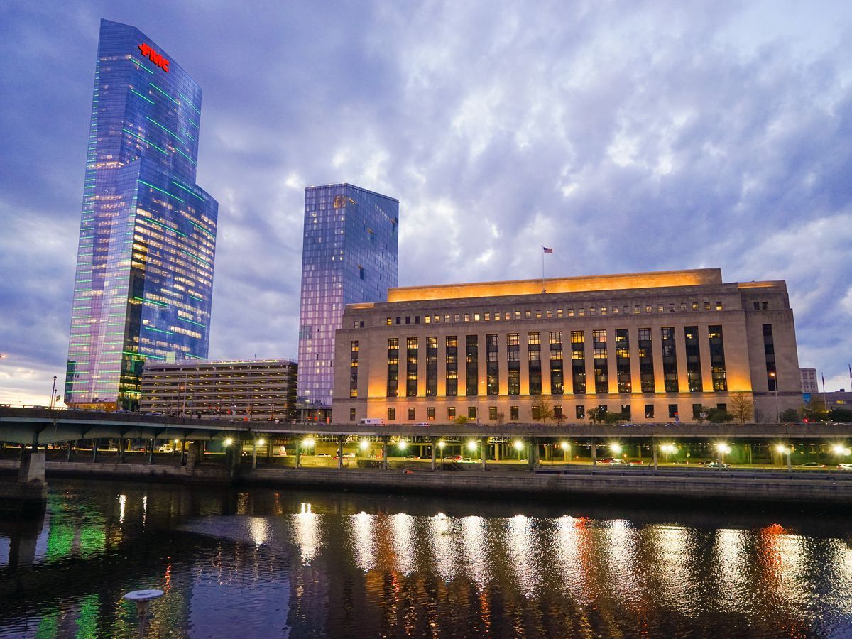 Philadelphia skyline at dusk; city buildings, reflecting in river below.