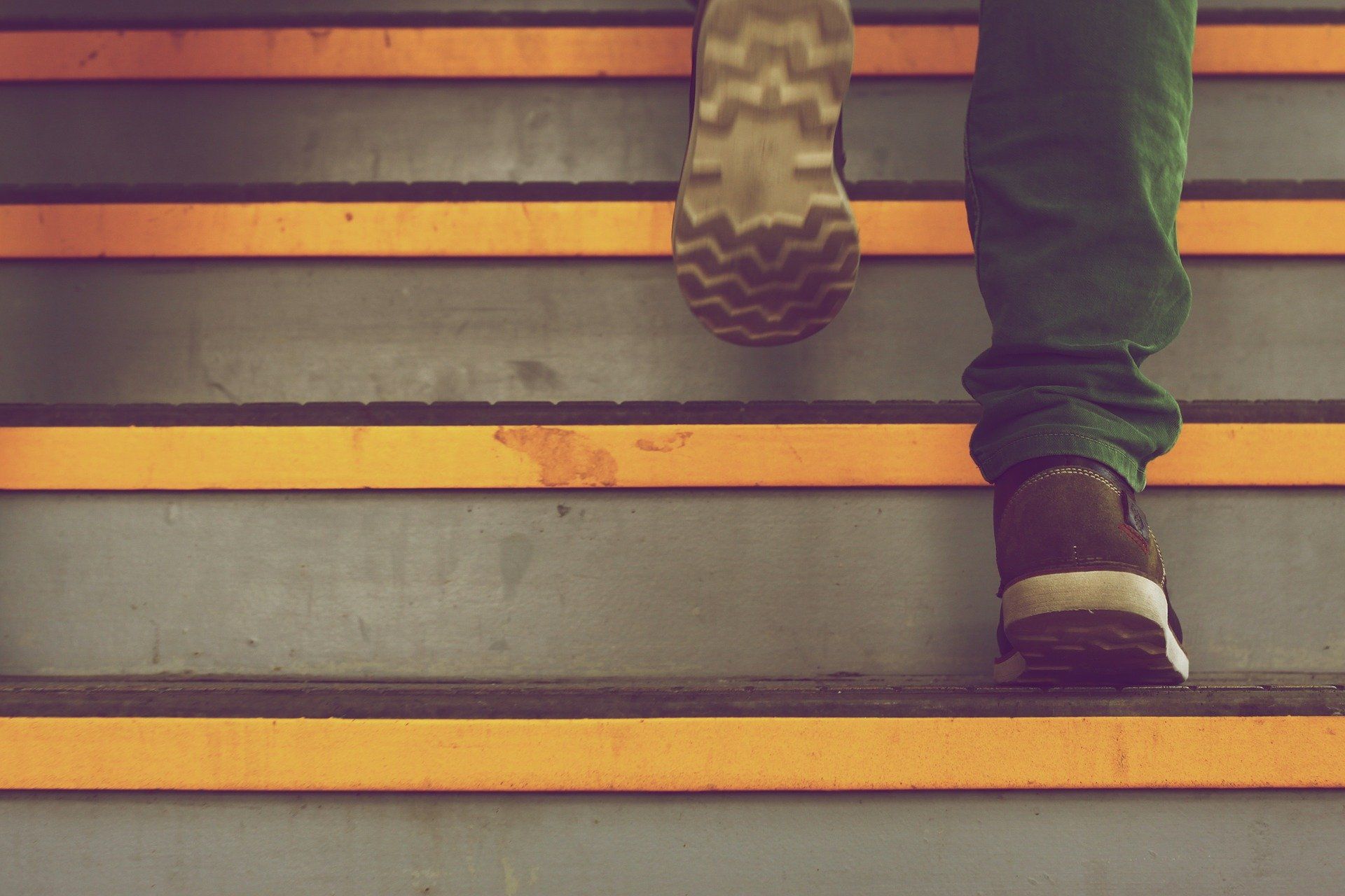 Person in green pants climbs gray stairs with orange stripes.