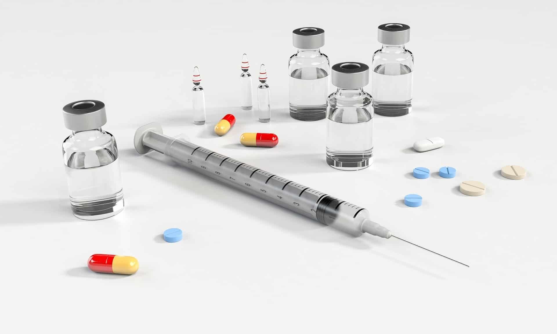 Syringe, vials, and pills on a white surface, medical supplies.