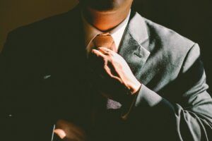 Man in suit adjusting tie, lit by sunlight.