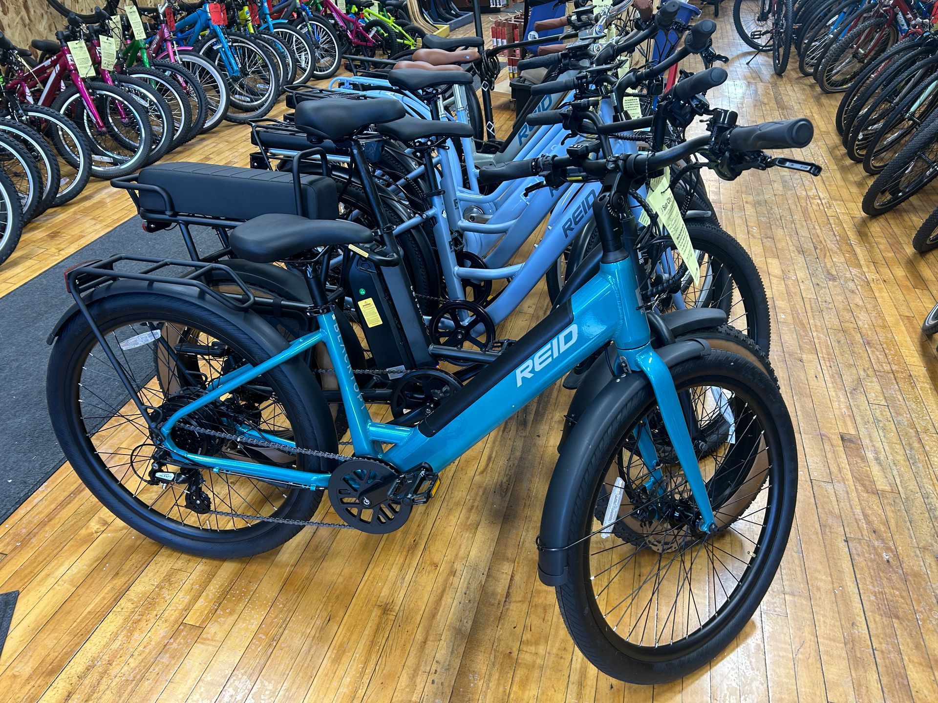 Blue electric bikes displayed in a bike shop with rows of bicycles in the background