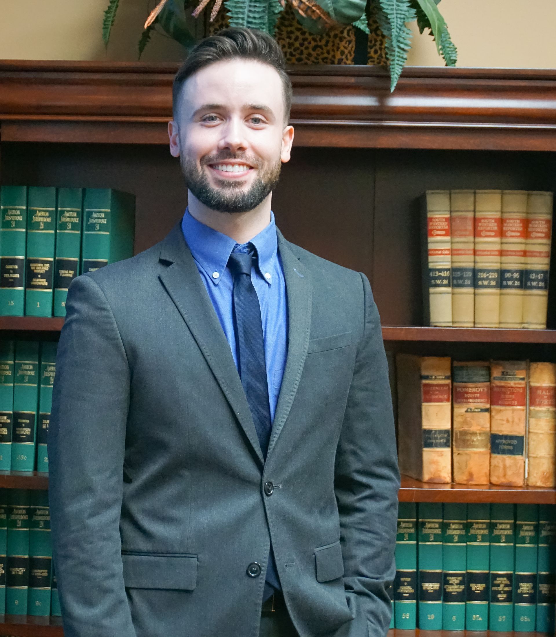 Man in suit smiling in front of a bookshelf filled with books.