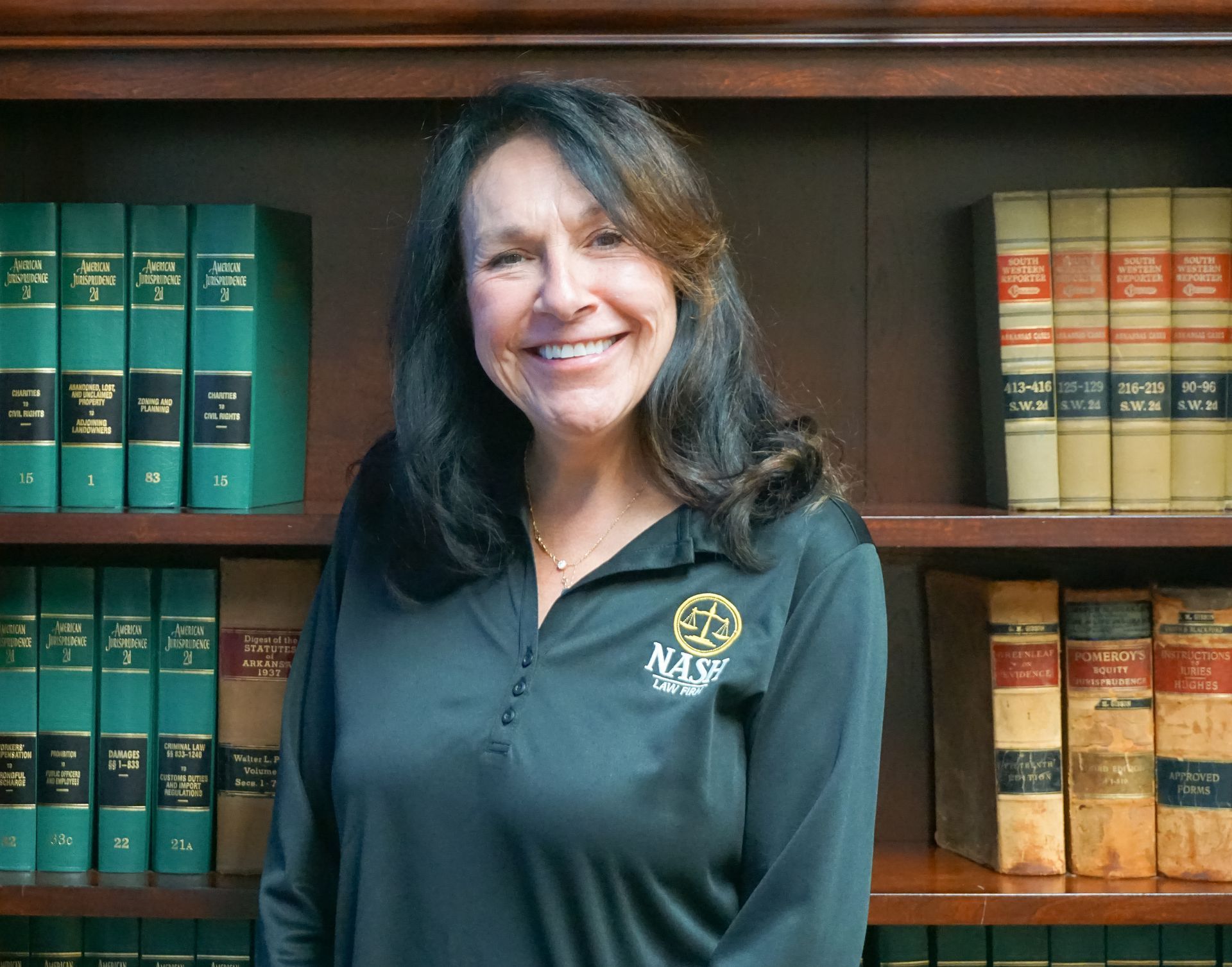Woman in black shirt smiles in front of a bookshelf filled with law books.