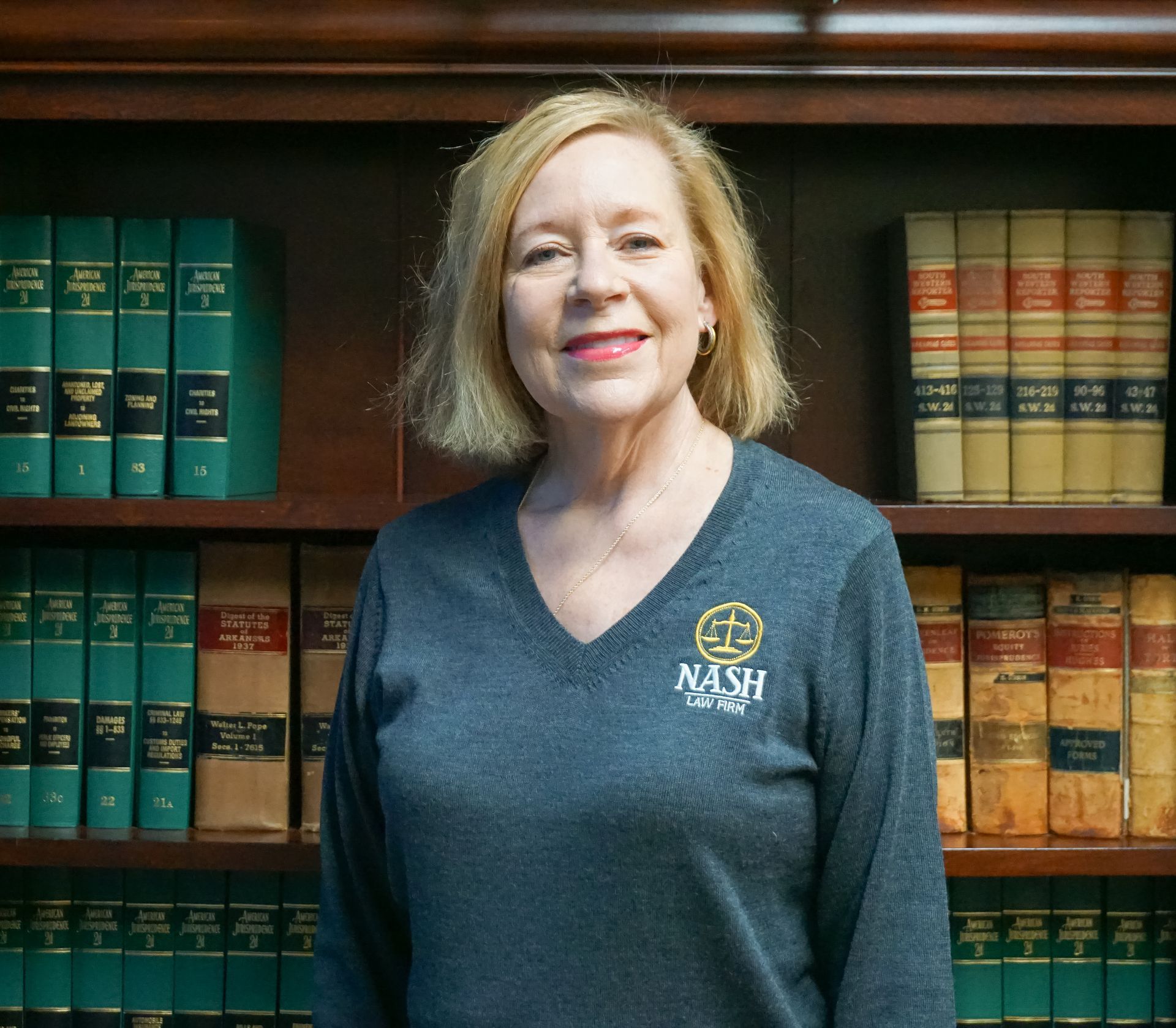 Woman in a gray sweater stands in front of a bookcase with legal volumes.