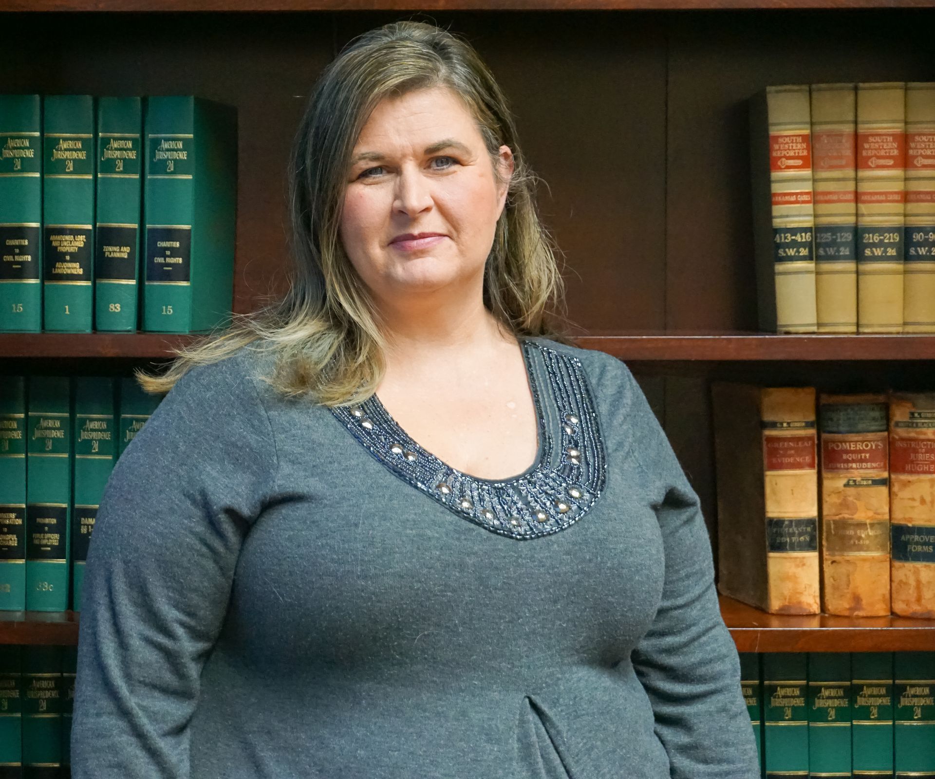 Woman in gray sweater stands in front of a bookcase filled with law books.