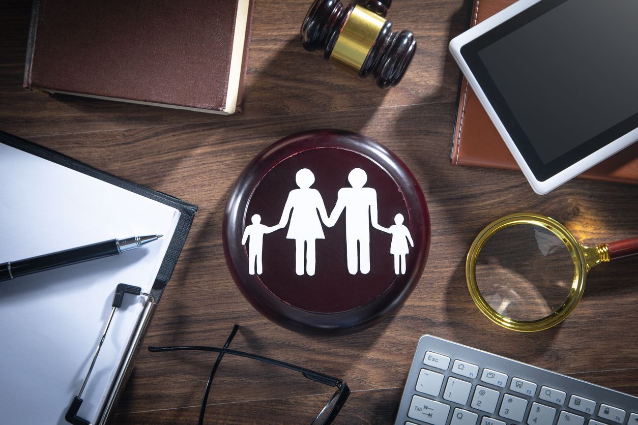 Family law concept: gavel, family icon, documents, tablet, keyboard, and magnifying glass on wooden desk.