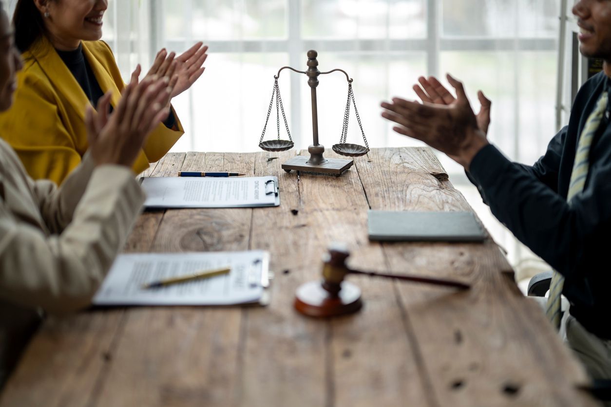 People applauding around a wooden table with scales of justice, gavel, and documents.