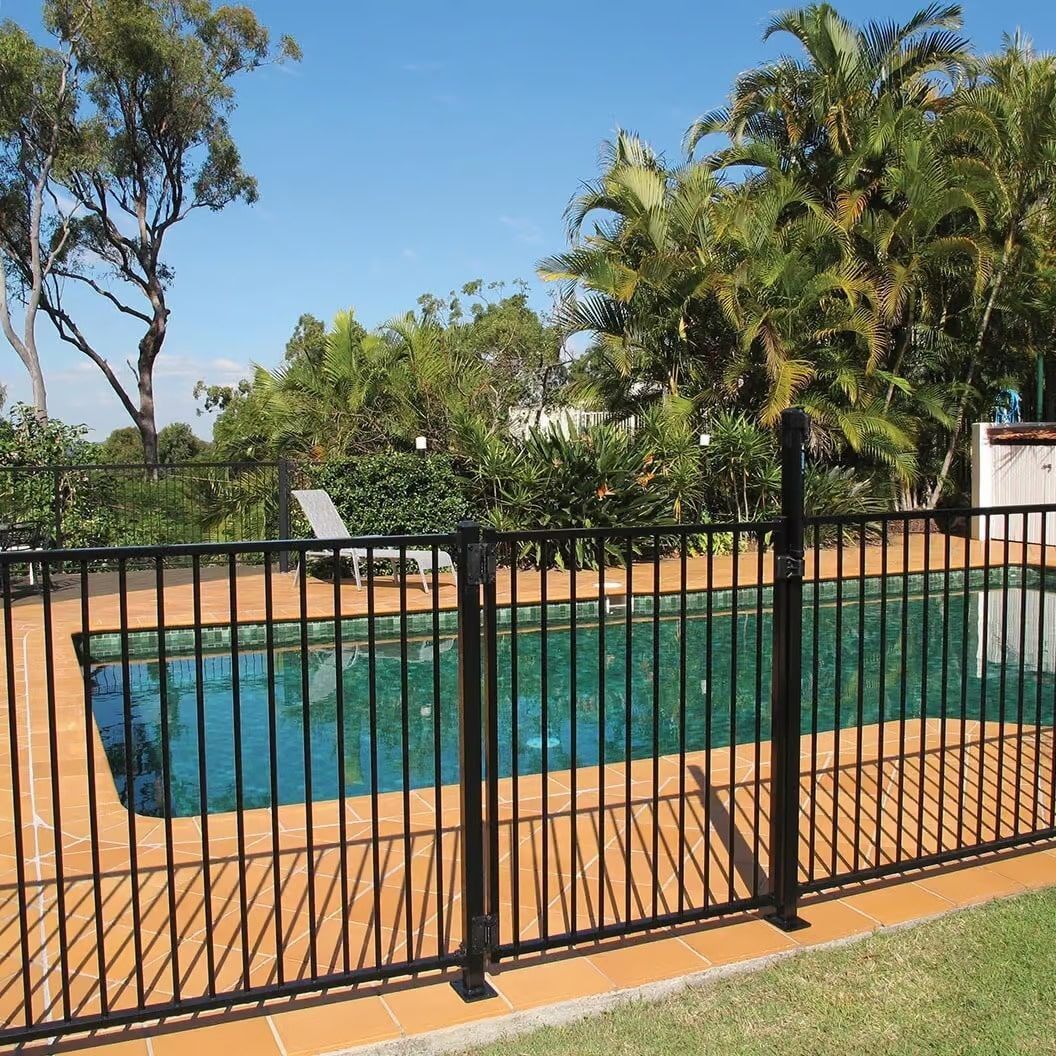 Black metal pool fence surrounds a blue swimming pool in a sunny backyard.