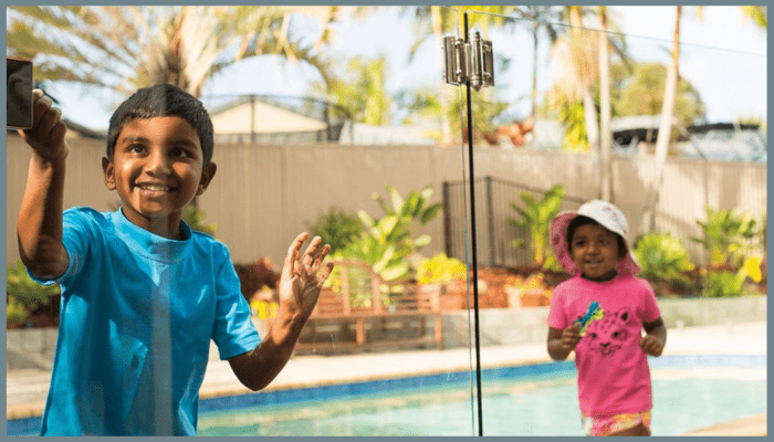 Two young children playing safely near a frameless glass pool fence