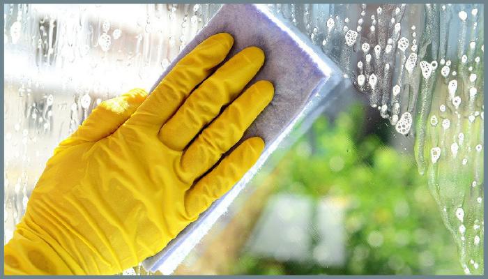Hand in yellow glove cleaning a glass pool fence with sponge for long-term maintenance and protection.
