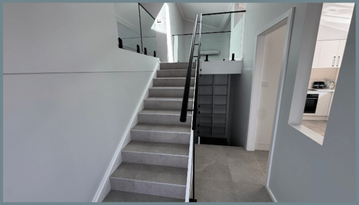 Modern staircase with compliant glass balustrade and black handrail meeting Australian safety standards in a Canberra home.
