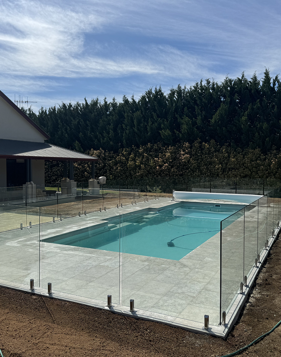 A large swimming pool is surrounded by a glass fence.