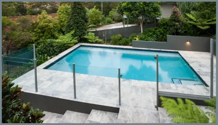 Frameless glass pool fencing on a sloped tiled surface in Canberra with stainless steel posts and lush landscaping.