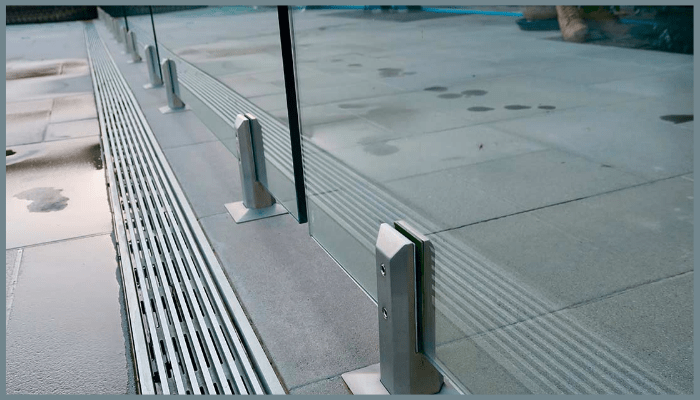 Close-up of frameless glass pool fencing with stainless steel spigots installed on tiled poolside in Canberra.